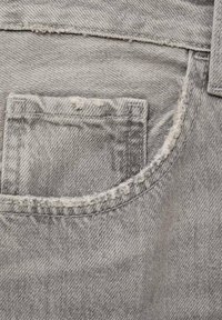 Sive denim tkanina z sprednjim žepom s frayed robovi, subtilno teksturo in vidnimi šivi.