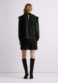 Abito nero strutturato con colletto a volant, apertura a chiave sul retro e gonna a strati. Abbinato a stivali alti in pelle nera.