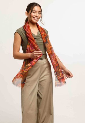 Multicolored scarf featuring wavy patterns in orange, red, and pink. Lightweight fabric with fringed edges, worn by a model.