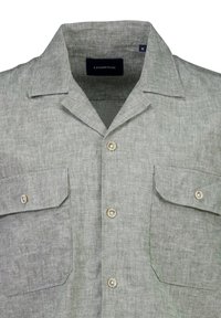 Camisa de manga corta gris claro con cuello tipo campamento, dos bolsillos en el pecho y cierre de botón. Hecha de una tela texturizada, presenta acentos de botones pálidos.