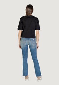 Maglietta nera a maniche corte e taglio cropped, abbinata a jeans flare azzurri chiari con una leggera sfumatura di lavaggio e un dettaglio del logo sul retro.