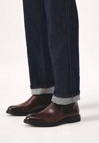Braune Leder Chelsea-Stiefel mit glatter Oberfläche, runder Zehenpartie und elastischen Seitenpaneelen, kombiniert mit hochgekrempelten dunkelblauen Jeans.