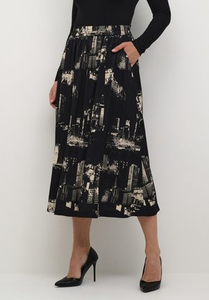 Schwarzer Midirock mit beigefarbenem Stadtbildmuster, elastischem Bund, Seitentaschen, getragen mit schwarzem Langarmshirt und schwarzen High Heels.