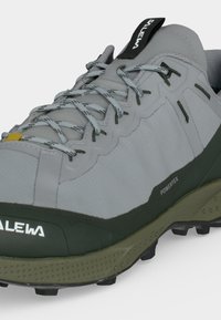Γκρι και πράσινο πεζοπορικό παπούτσι με μοτίβο στα κορδόνια, ανθεκτική σόλα και ορατό όνομα μάρκας "Salewa" στη γλώσσα και στην πλευρά.