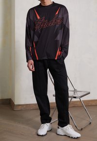 Svart idrottströja med röda detaljer och grafisk text, kombinerad med svarta byxor och vita sneakers. Slät tygkvalitet med en avslappnad passform.