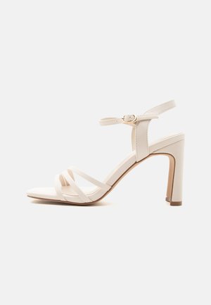 Beige High-Heel-Sandalette mit drei dünnen vorderen Riemen, Knöchelriemen mit goldener Schnalle und Blockabsatz auf weißem Hintergrund.