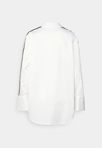 Vit långärmad skjorta med krage, rundad nederkant och svarta och guldstrimmiga detaljer på axlarna. Slät bomullstyg.