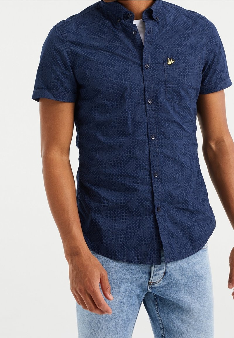Námořnicky modrá košile s krátkými rukávy, texturovaným vzorem, límečkem na knoflíky a malým vyšívaným logem na kapse na prsou.
