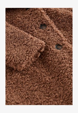 Brūns teksturēts vilnas mētelis ar pūkainu virsmu, lieliem pogām un pārklājošām krokām pie apkakles un priekšpuses.