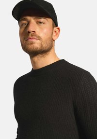 Černý svetr s texturou a kulatým výstřihem, doplněný černou kordovou čepicí. Zaměřte se na tkaný vzor svetru.