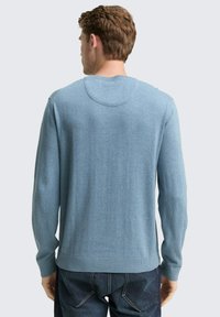 Hellblaues Strickoberteil, lange Ärmel, gerippte Bündchen und Saum, runder Halsausschnitt, glatte Textur, kombiniert mit dunklen Denim-Jeans.