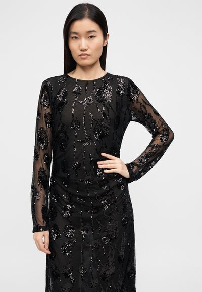 Must kleit läbipaistvast kangast, pika varruka ja tikitud lillemustrite ning litritega kaunistatud, keha järgiva lõikega.