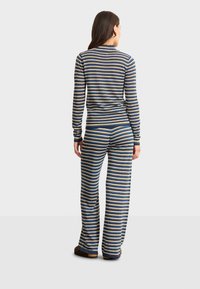 Gestreept loungewear-set met een langemmouwen top en pants. Materiaal lijkt zacht met marineblauwe, roomkleurige en gouden strepen. Aansluitend en ontspannen ontwerp.