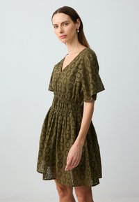 Kurzes olivgrünes Kleid mit Lochmuster, V-Ausschnitt, Puffärmeln und elastischem Taillenbund; fließender Rock mit lässiger Passform.