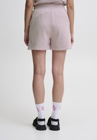 Světle růžové kraťasy vyrobené z měkké tkaniny, se stahovacími kalhotami v pase, kombinované s bílými ponožkami a černými sandály. Jednoduchý design bez vzorů.