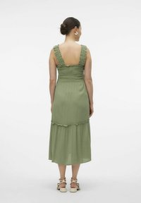 Vestido midi verde oliva con tirantes con volantes, un cuerpo ajustado y una falda en capas. Hecho de una tela ligera con una textura suave.