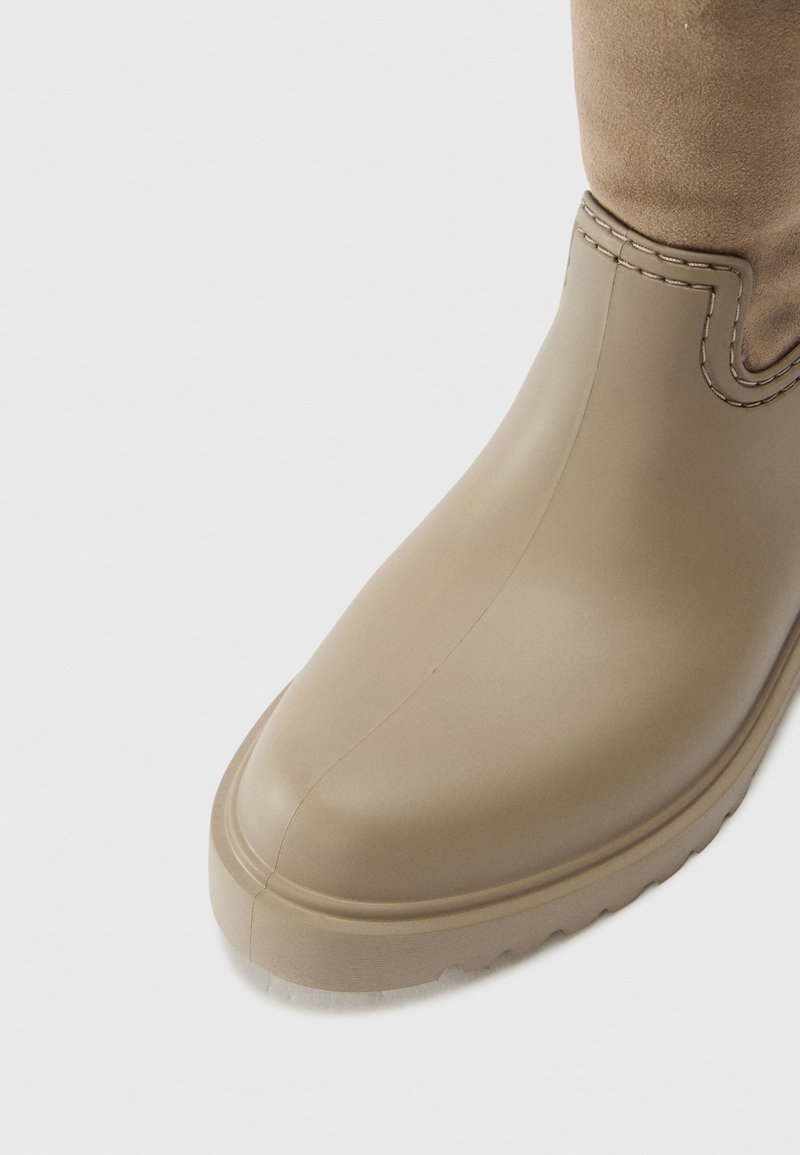 Botín impermeable color marrón, con material de goma suave, punta redonda y parte superior de ante cosida, que cuenta con una suela texturizada.