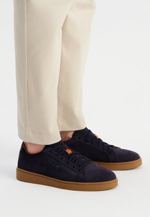 Granatowe zamszowe sneakersy z gumowymi podeszwami, z czarnymi sznurówkami i kolorowym akcentem po bokach. Casualowy niski design.