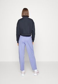 Schwarzer, kurz geschnittener Sweatshirt mit strukturierten Ärmeln, kombiniert mit hellvioletten Jogginghosen und weißen Turnschuhen, Rückansicht.