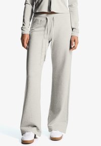 Világosszürke, kényelmes szabású melegítőnadrág, rugalmas derékkal és húzózsinórral. Simább anyag, oldalsó zsebekkel és hozzáillő cipőkkel.