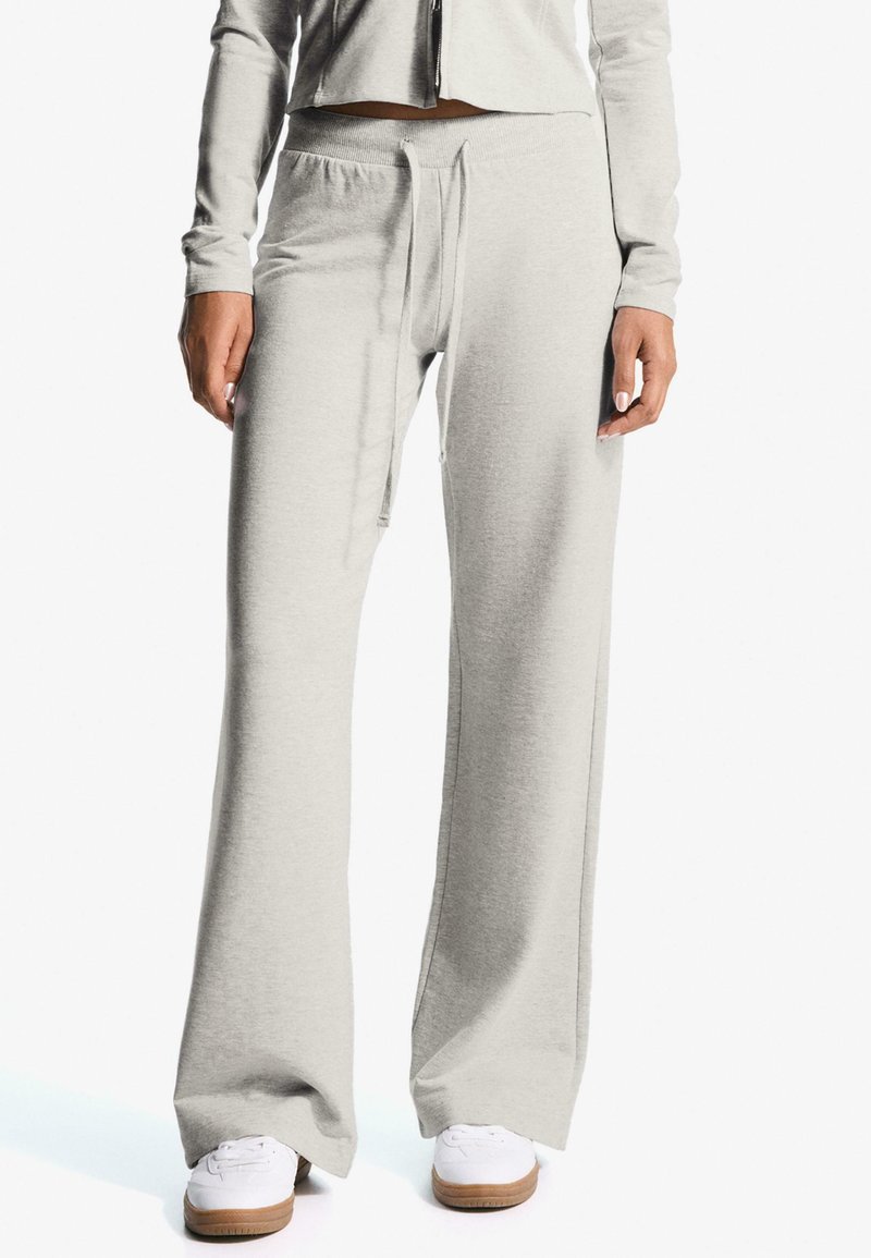 Világosszürke, kényelmes szabású melegítőnadrág, rugalmas derékkal és húzózsinórral. Simább anyag, oldalsó zsebekkel és hozzáillő cipőkkel.