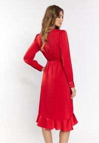 Rochie din satin roșu cu m�âneci lungi, talie strânsă și margine cu volane. Prezintă accente cu nasturi pe mâneci și o textură netedă, lucioasă.