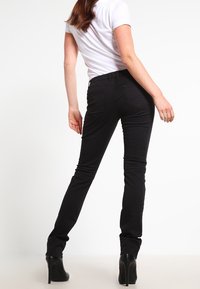 Svarta slim-fit jeans med en slät textur och minimala sömnadsdetaljer, tillsammans med en vit t-shirt och svarta högklackade skor.