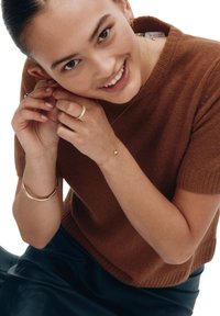 Brown ribbed knit sweater with short sleeves, paired with a black leather skirt. Accessories include gold bangles, rings, and a delicate necklace.