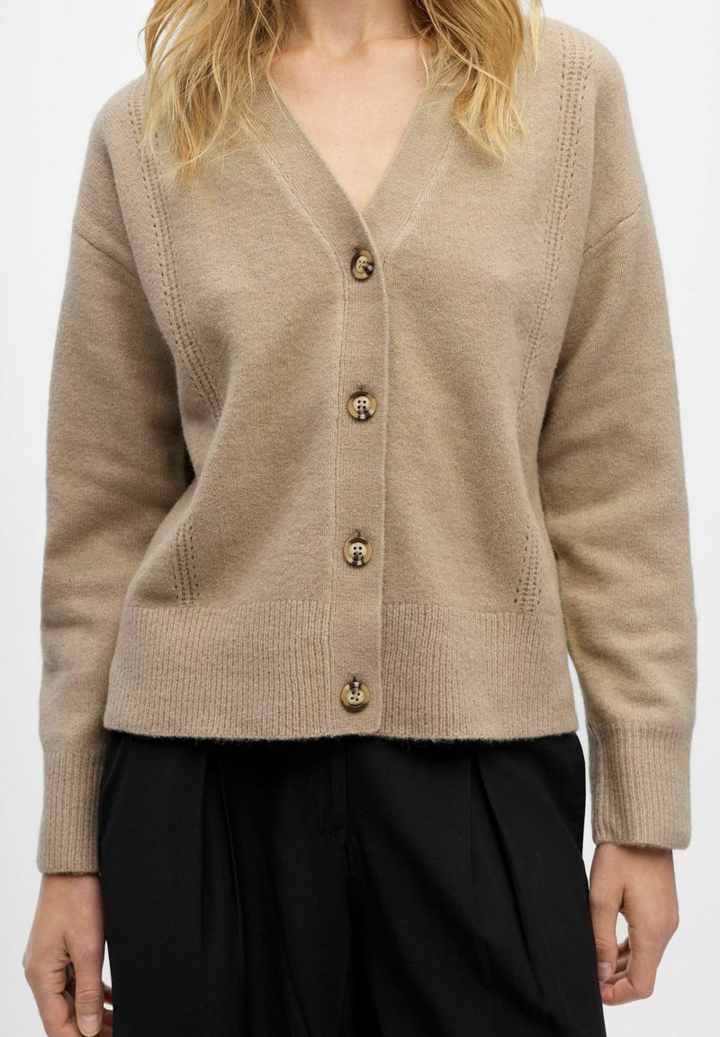 Beige wool cardigan with a V-neck, featuring six brown buttons, ribbed hem, and subtle vertical stitch detailing along the seams.