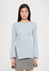 Light blue ribbed knit sweater with long sleeves and flared cuffs, paired with a checkered skirt, featuring a straight cut and slight side splits.