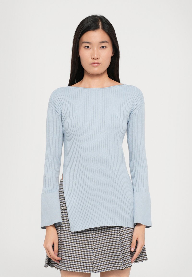 Light blue ribbed knit sweater with long sleeves and flared cuffs, paired with a checkered skirt, featuring a straight cut and slight side splits.