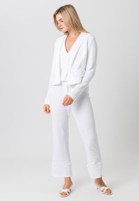 Witte gebreide jas met structuur, in een getailleerde pasvorm en met gescheurde revers, gecombineerd met hoog getailleerde witte broek met uitlopende mouwen.