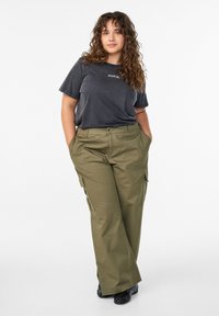 Olivzaļas krāsas darba bikses ar sānu kabatām, kombinētas ar tumši pelēku T-kreklu ar uzrakstu "PRIECĪGS" baltā krāsā. Gluda tekstūra.