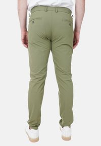 Pantaloni khaki con una vestibilità slim, vita elastica e due tasche posteriori con chiusure a bottone, abbinati a scarpe bianche e una superficie liscia.