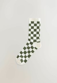 Enkele witte sok met een donkergroen geblokt patroon plat gelegd op een lichte achtergrond.