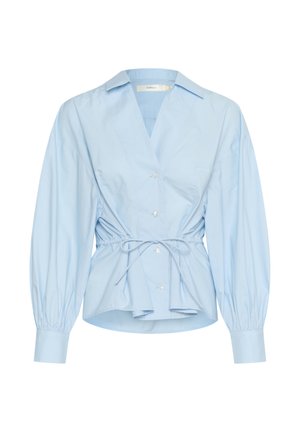 Blusa avvolgente blu chiaro in cotone con scollatura a V profonda, vita elasticizzata e maniche a palloncino. Presenta cinque bottoni sul davanti.