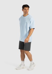 T-shirt oversized bleu clair avec des manches courtes, un col rond et un petit logo, associé à un short gris foncé et des baskets blanches.