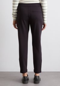 Zwarte, op maat gemaakte broek met een gladde textuur, elastische taille en één achterzak, gecombineerd met zwarte platform schoenen.