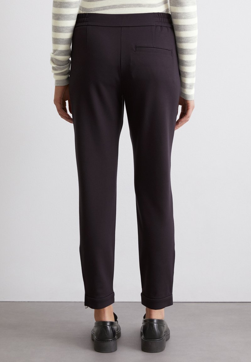 Schwarze, maßgeschneiderte Hosen mit glatter Textur, elastischem Bund und einer einzigen Gesäßtasche, kombiniert mit schwarzen Plateau-Schuhen.