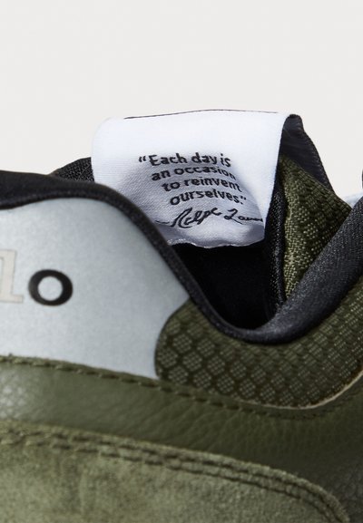 Groene en grijze sneaker met een gemusterde mesh-tong, leren en suède materialen, en een label met een citaat dat aan de binnenkant is gestikt.