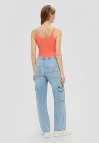 Koralle geripptes Tanktop kombiniert mit hellblauen Cargo-Hosen. Die Hosen haben zwei Gesäßtaschen und seitliche Cargotaschen. Das Model trägt weiße Sneakers.