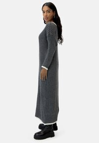 Vestido largo gris de punto acanalado con silueta ajustada y puños blancos en contraste. Combinado con botas negras de plataforma.