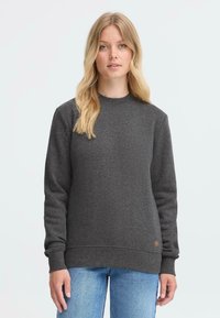 Mørkegrå hettegenser med rund hals, ribbestrikkede ermer og nederkant. Har en liten brun logo-patch på den nedre siden. Uformell design.