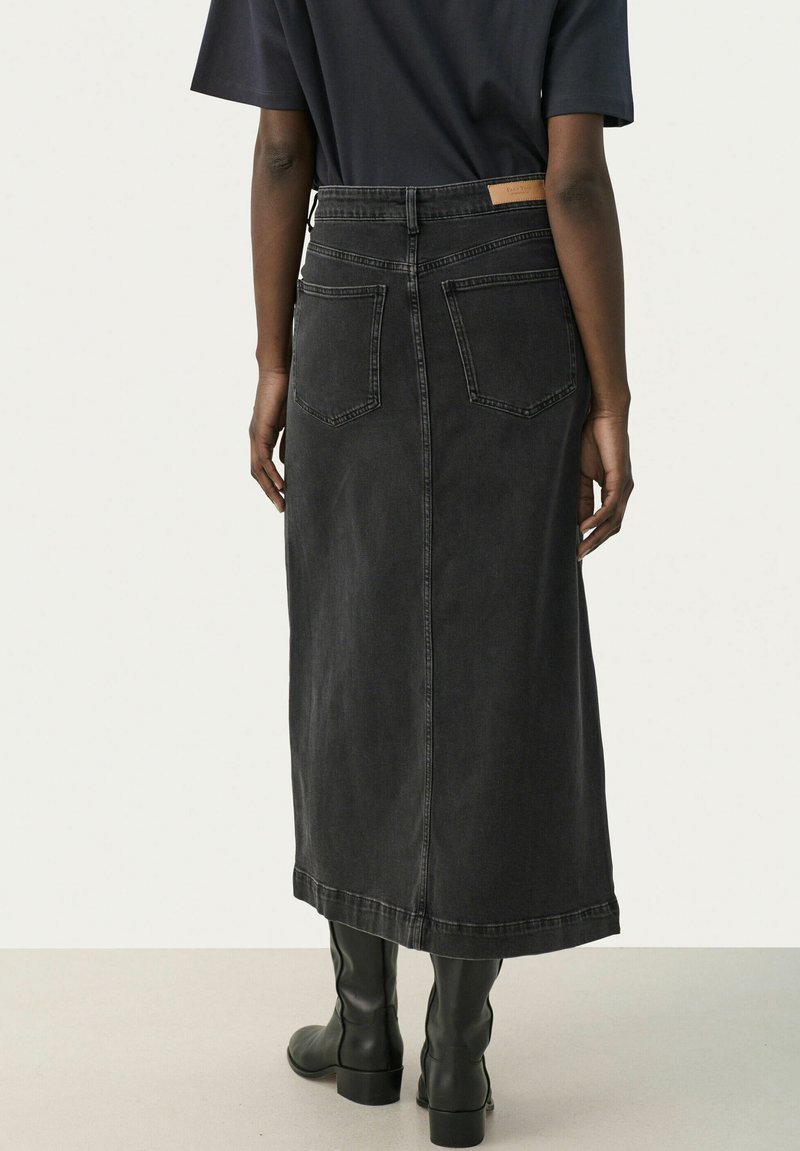 Czarna jeansowa spódnica midi z tylnymi kieszeniami, widocznym szwem i brązową metką na pasku. W zestawie z czarnymi botkami do kolan.