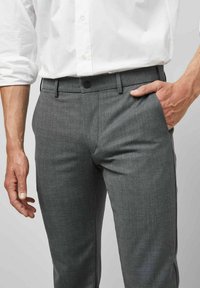 Graue maßgeschneiderte Hose aus strukturiertem Stoff, slim fit, mit Seitentaschen und Knopfverschluss. Kombiniert mit einem weißen Hemd.
