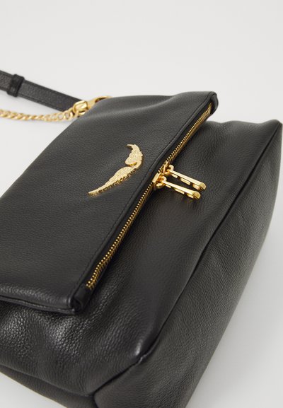 Borsa a mano in pelle nera con superficie testurizzata, caratterizzata da una cerniera dorata e tiranti per cerniera dorati, e un emblema decorativo dorato sul davanti.