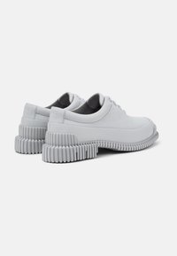 Baskets grises à lacets avec un bout arrondi, une semelle épaisse côtelée, une tige en cuir lisse et une doublure intérieure rembourrée.