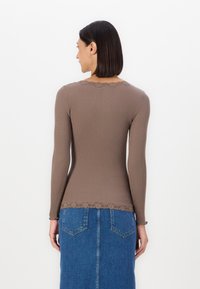 Pruun ribaga pikade käistega blousee, millel on laineline pitsist äär, koos denim seelikuga. Blouseel on istuv lõige ja ümmargune kaelus.