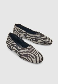 Een paar platte instapschoenen met zwart-wit zebra print patroon en puntige neuzen op een lichtgrijze achtergrond.