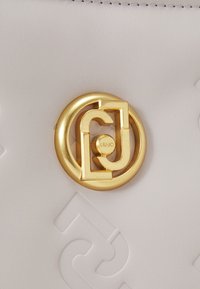 Cuir gris clair avec motif en relief ; caractéristiques d'un fermoir circulaire doré avec les initiales entrelacées "LJ," détaillé par une gravure "LIU-JO."